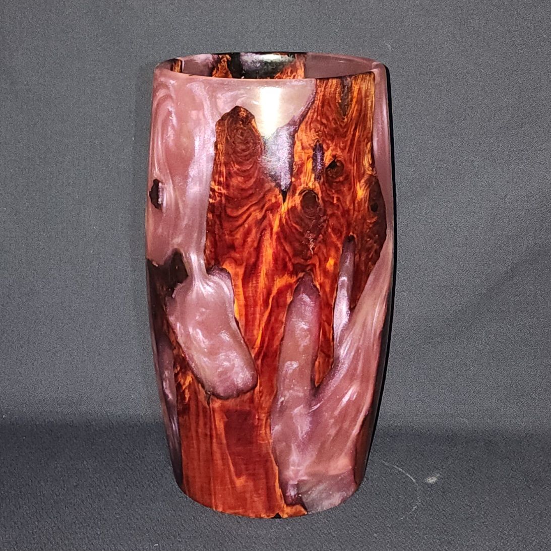Vase made of wood and pink resin, with a dark wood grain pattern on a gray background.