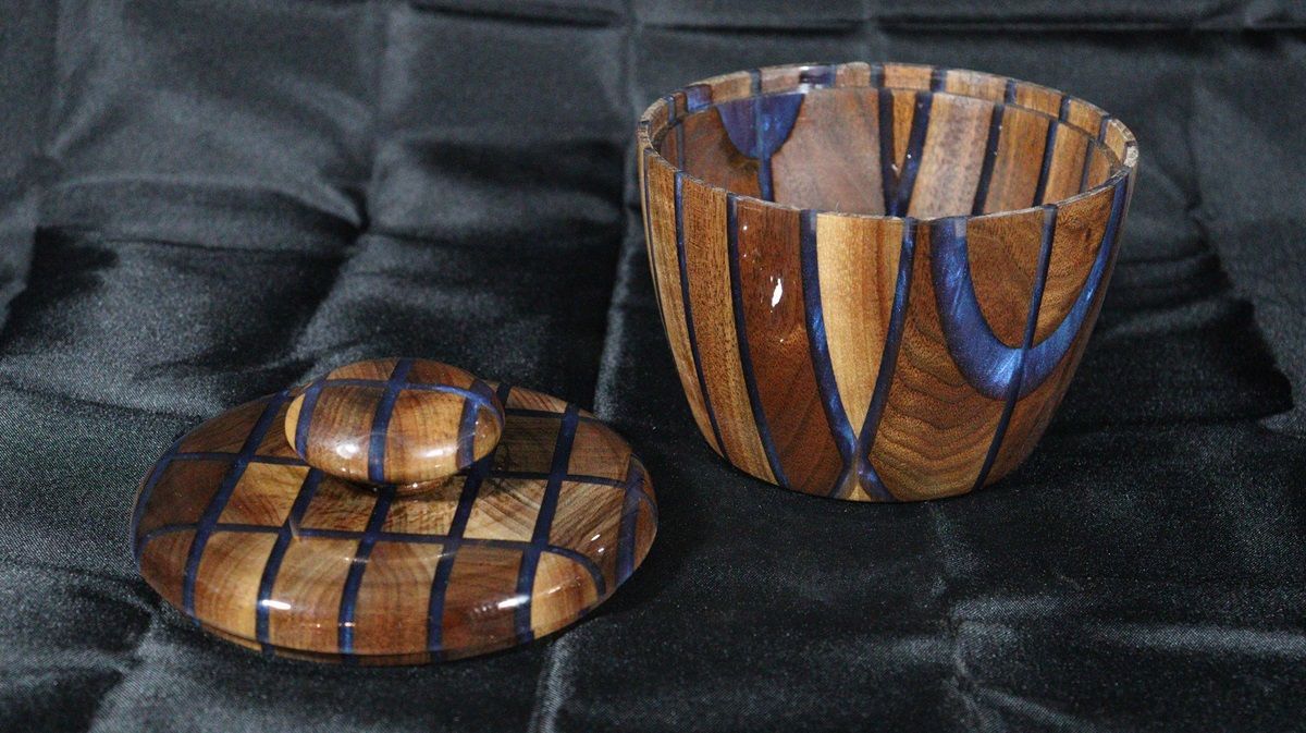 Wooden bowl with lid; brown and blue pattern on a dark textured surface.