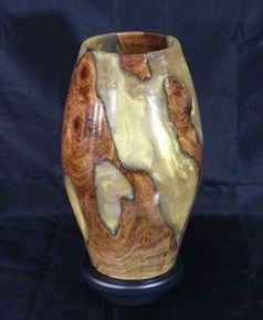 Wooden vase with brown and gold grain patterns on a dark pedestal.