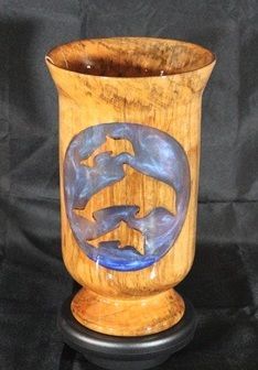 Wooden vase with dolphin cutout filled with blue resin, on a black base.