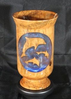 Wooden vase with three bat cutouts, filled with blue resin. Brown, on a black stand.