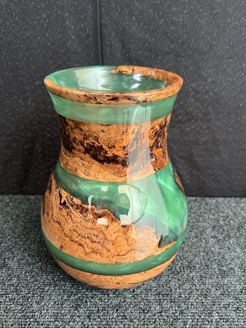 Wood and green resin vase, brown textured wood with green translucent resin, displayed on a dark surface.