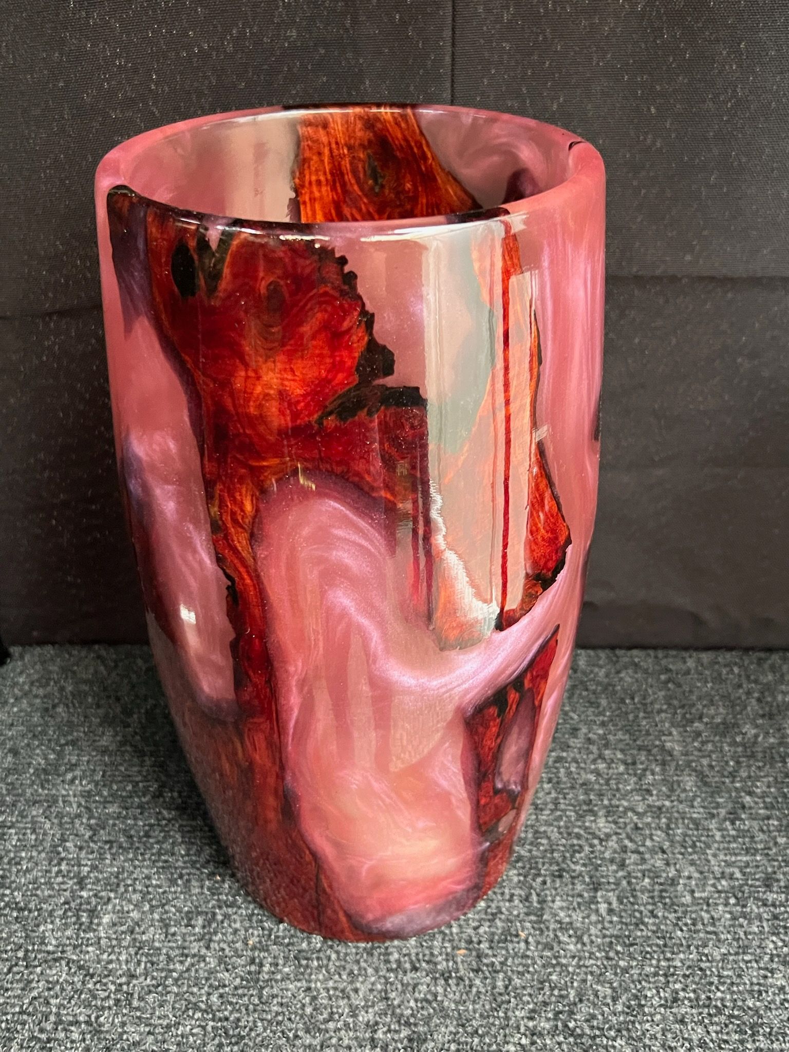 Pink and red resin vase with wood inclusions, in front of a dark background.
