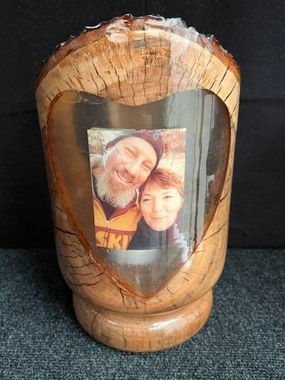 Wooden urn with a heart-shaped window, displaying a smiling couple's photo.