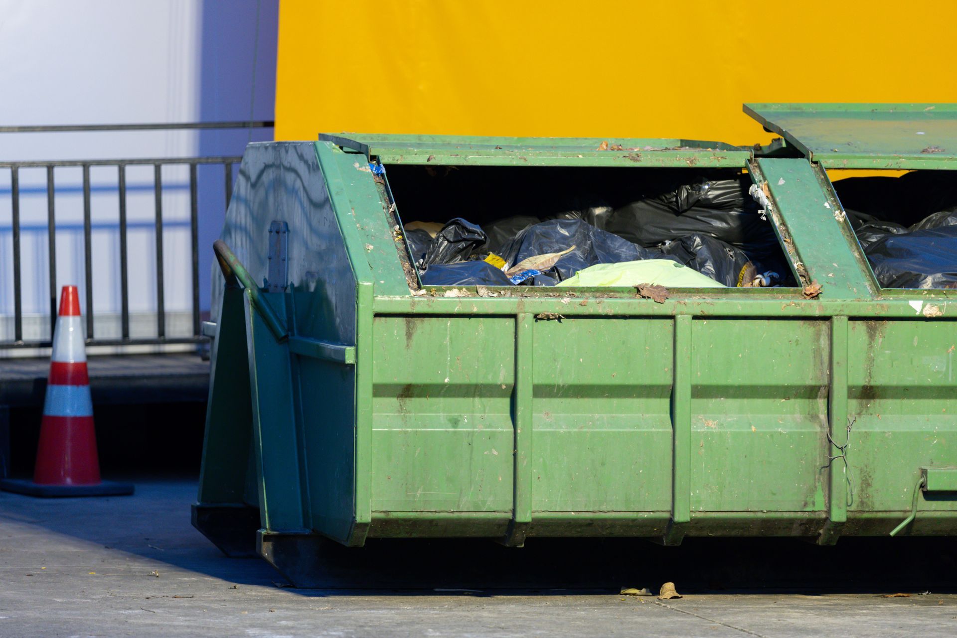 Large green dumpster filled with black trash bags ready for local garbage removal services.