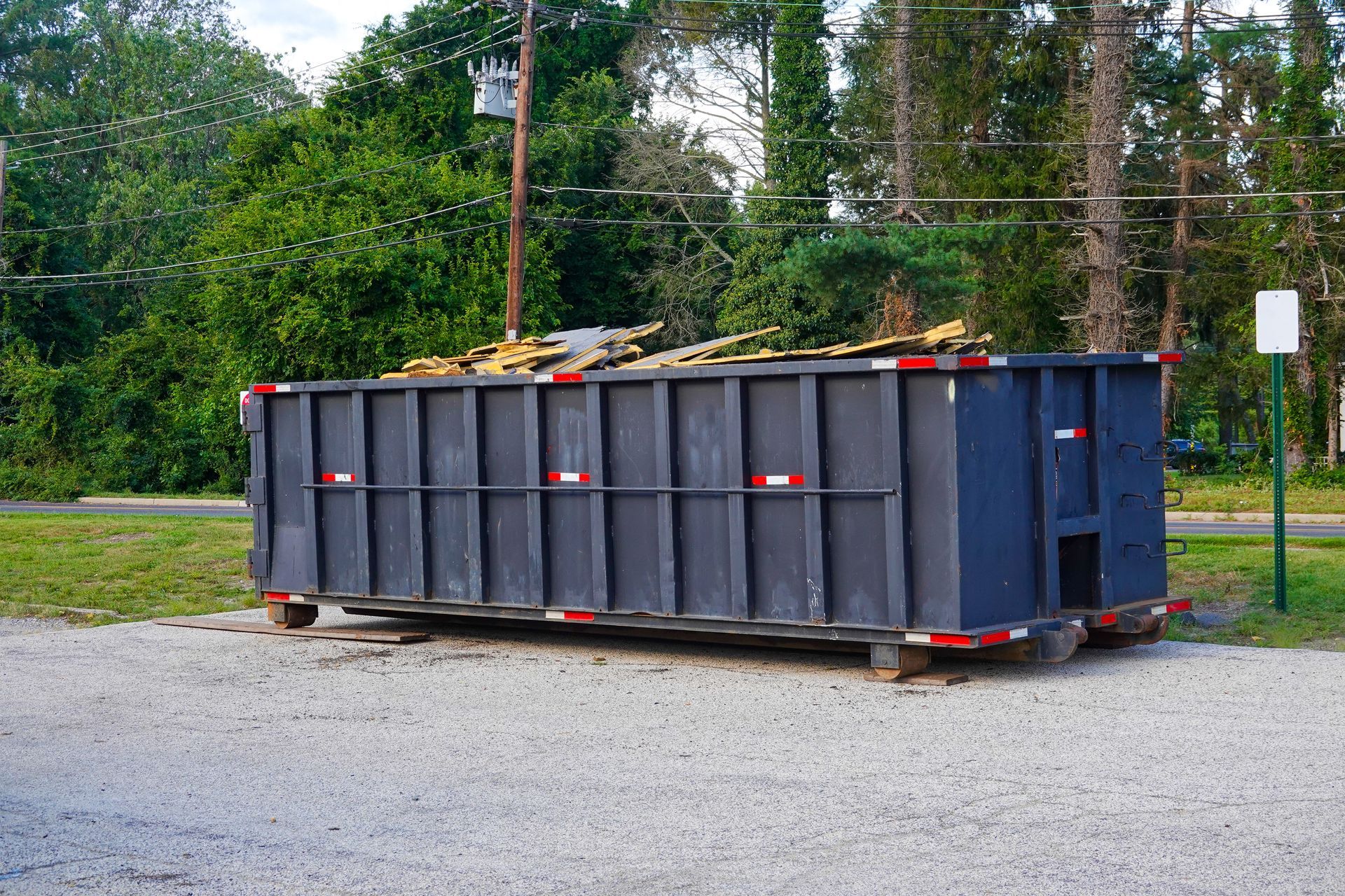 Photograph of a large, dark gray dumpster placed on a gravel surface 
