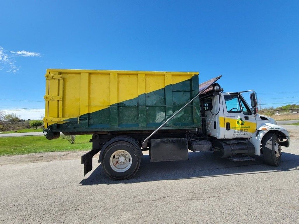 A yellow and green dump truck is parked roadside under a clear blue sky A yellow and green dump truck is parked roadside under a clear blue sky