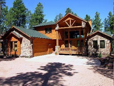 A large wooden house with a green roof is surrounded by trees