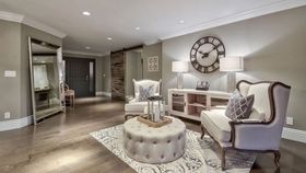 A living room with a couch , chairs , ottoman and a clock on the wall.
