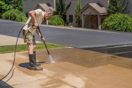 Man pressure washing base of concrete driveway in Moore OK home