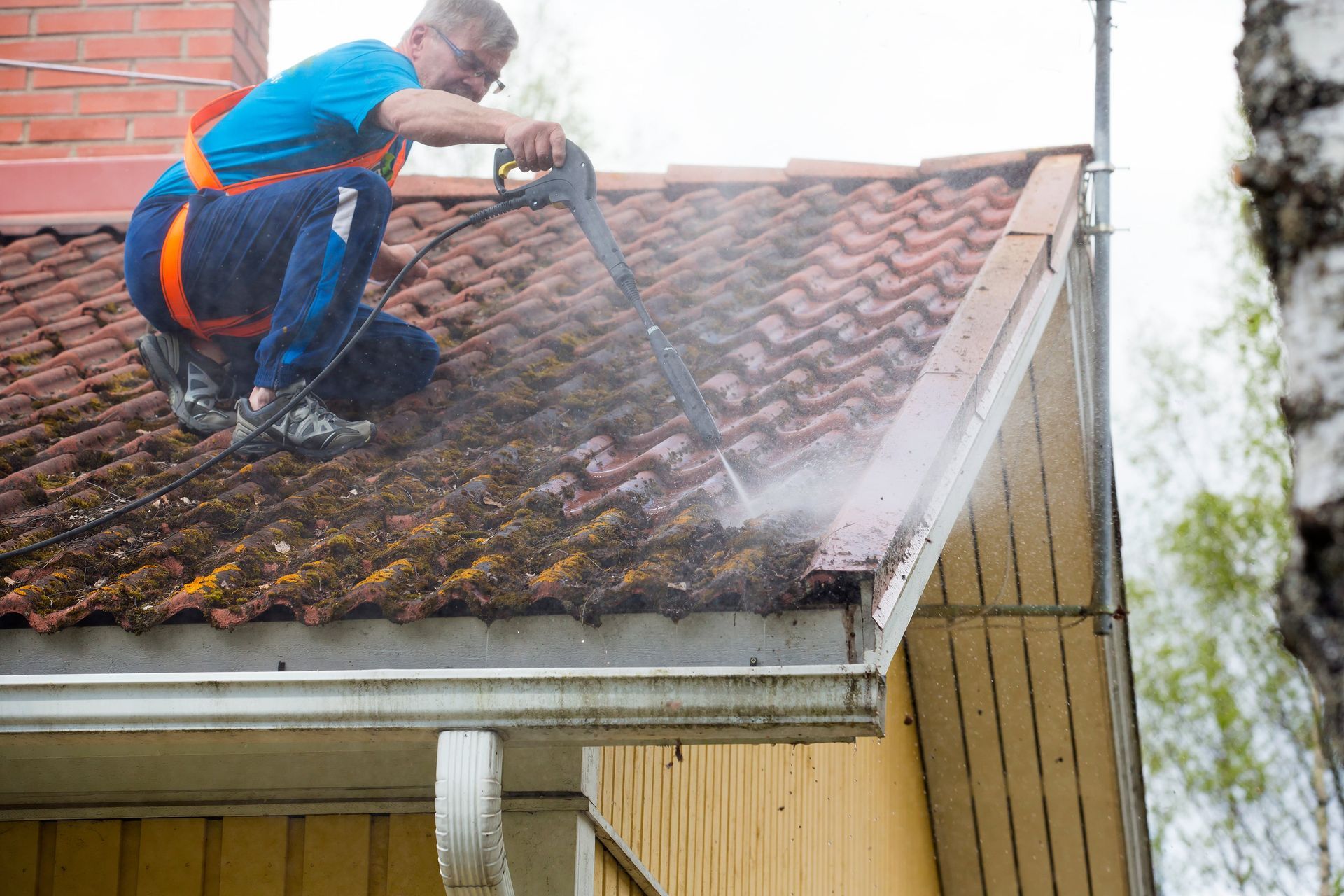 Man on roof power washing roof tiles