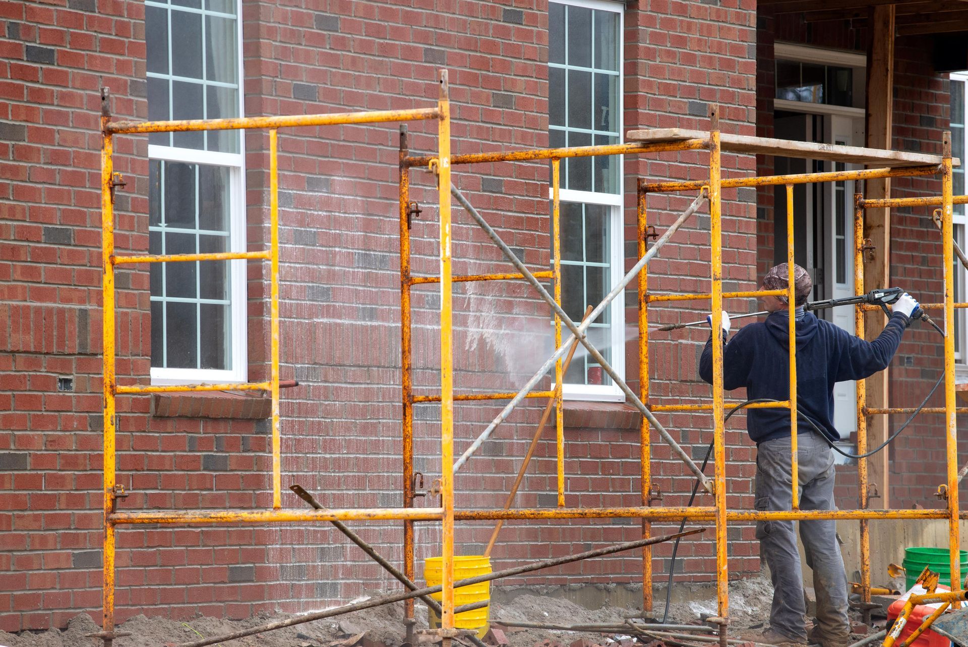 Man in scaffolding power washing windows