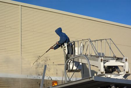 Worker on lift pressure washing front of commercial building near downtown OKC
