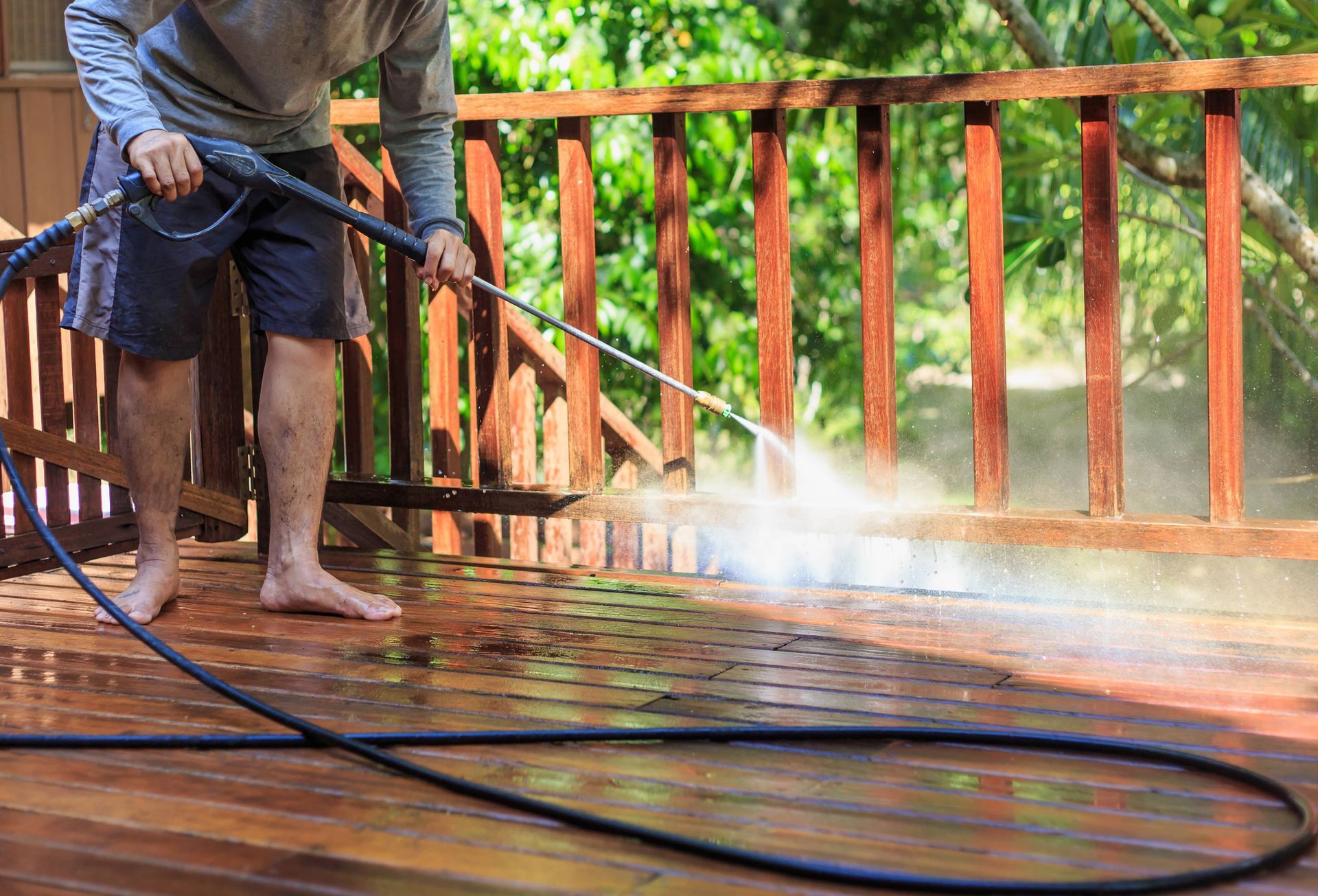 Man pressure washing wooden deck in backyard