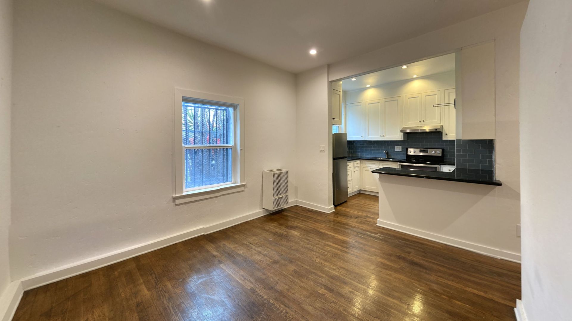 Empty apartment interior with hardwood floors and open kitchen.