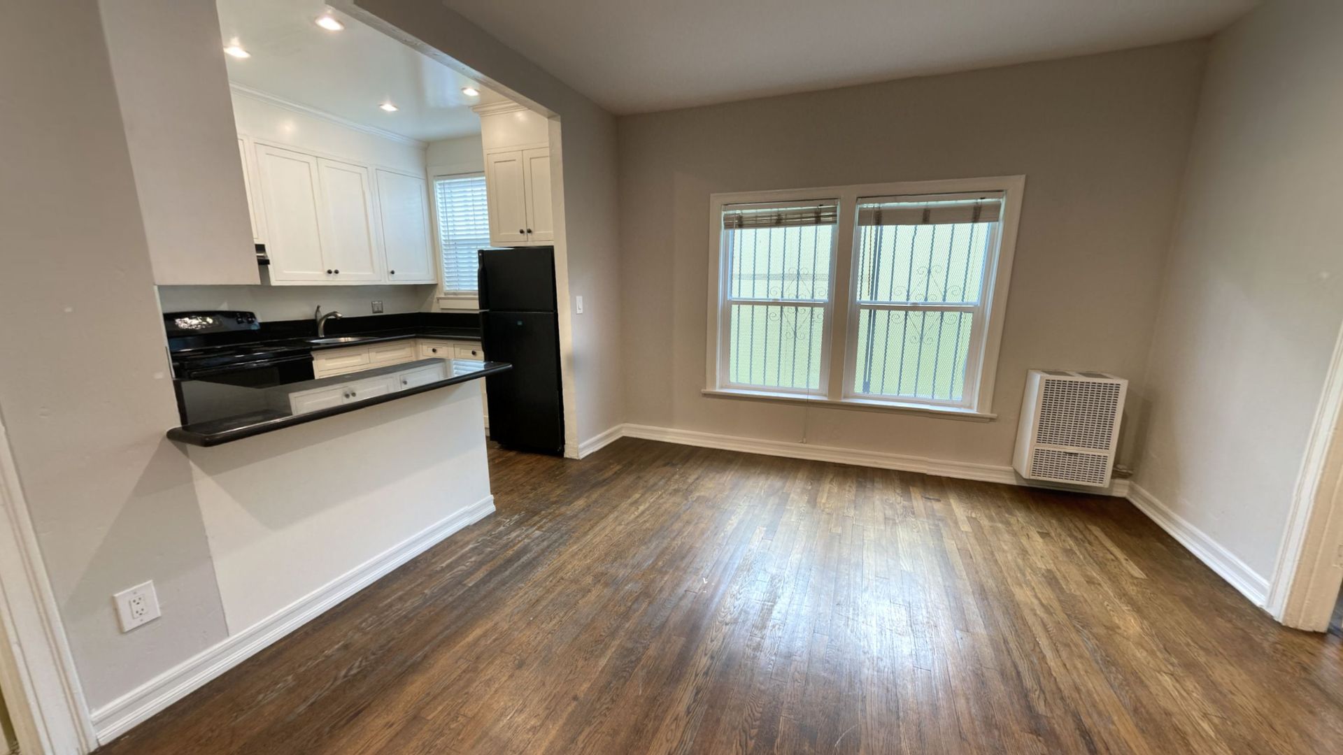 Dining room with hardwood floors, window with bars, and kitchen entrance.