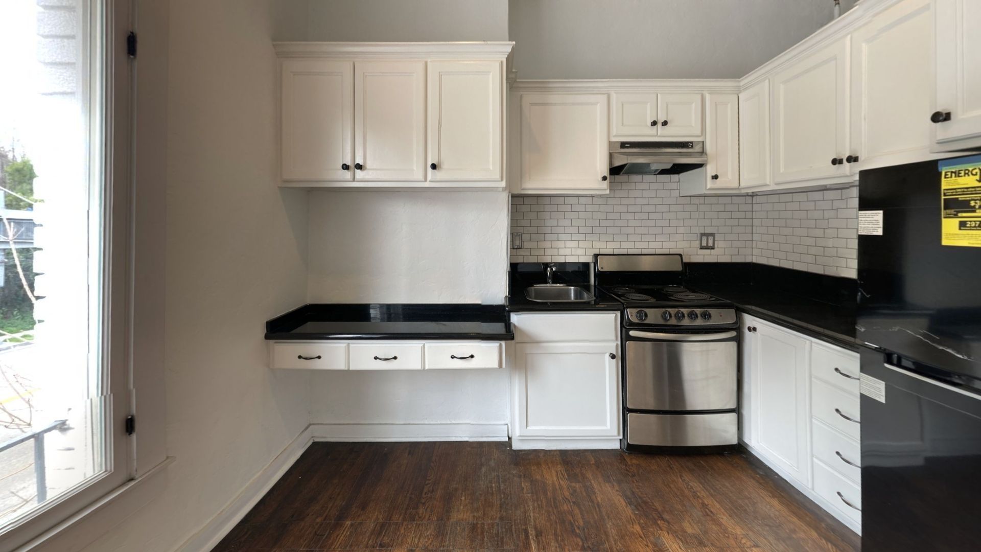 Kitchen with white cabinets, black countertops, stainless steel appliances, and wood floors.