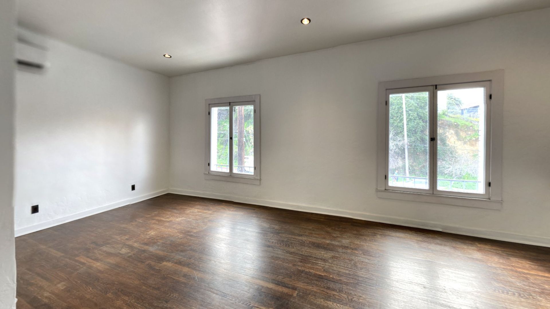 Empty room with hardwood floors, two windows, and white walls.