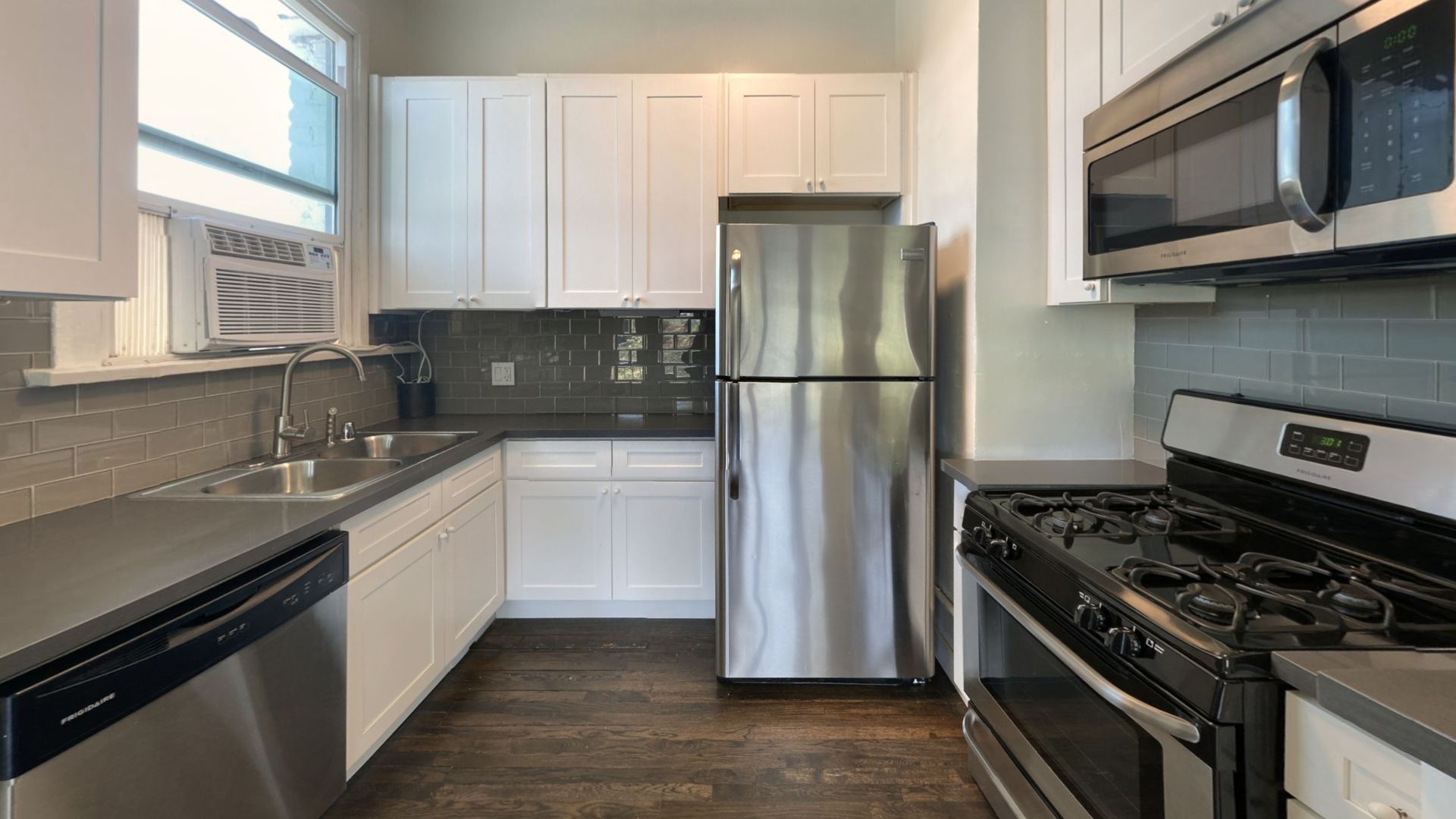 Kitchen with stainless steel appliances, white cabinets, grey counters, and dark wood floor.