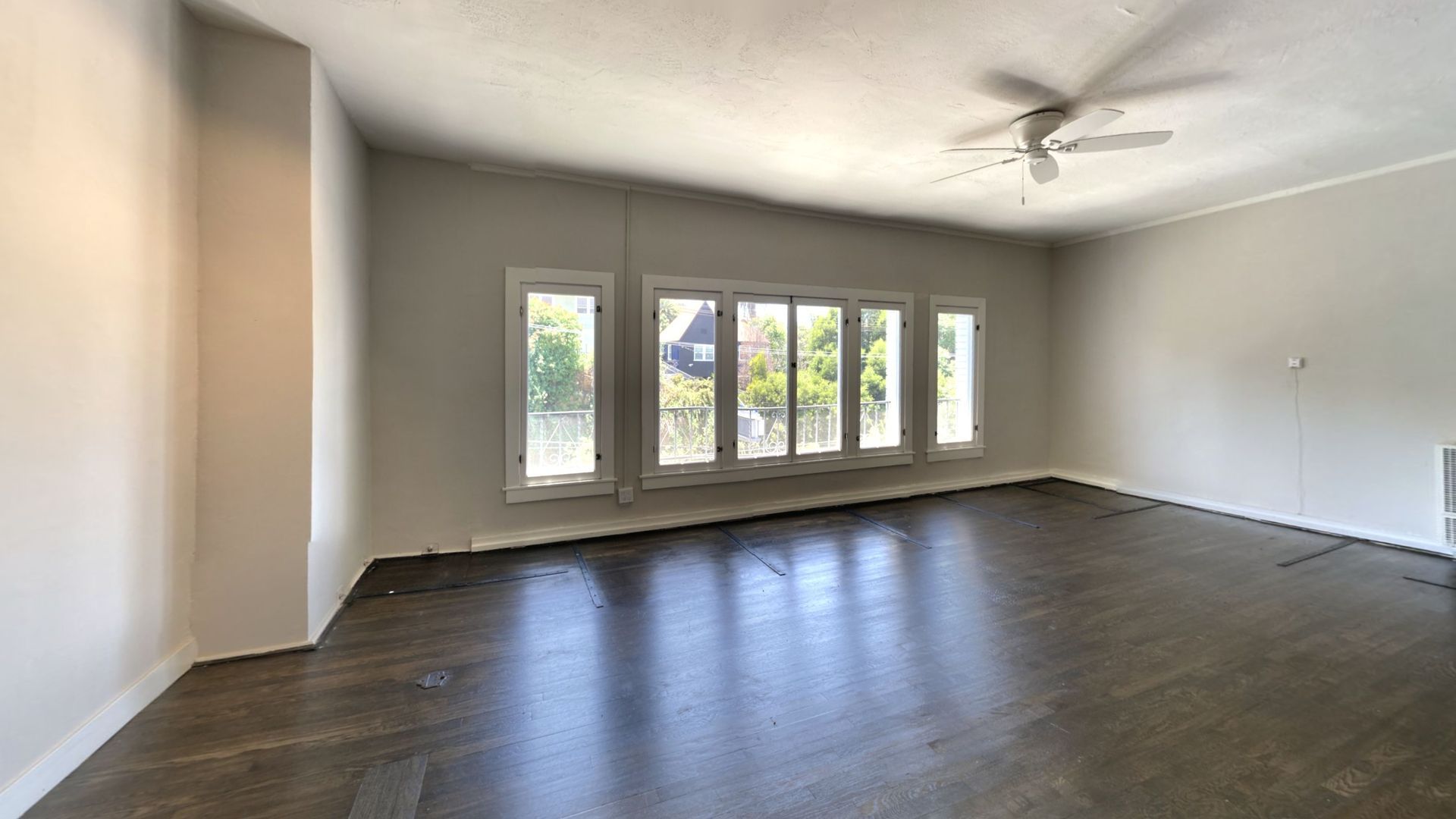Empty room with hardwood floors, a bank of windows, and a ceiling fan.