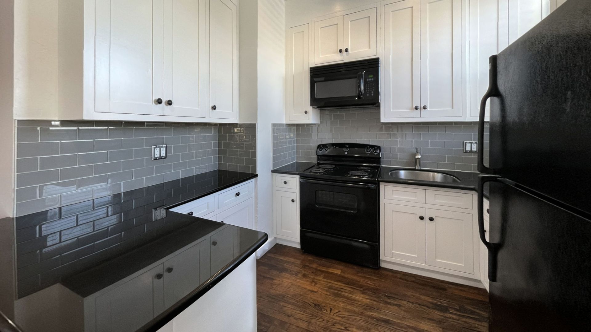 White kitchen with black appliances, counters, and gray subway tile backsplash.