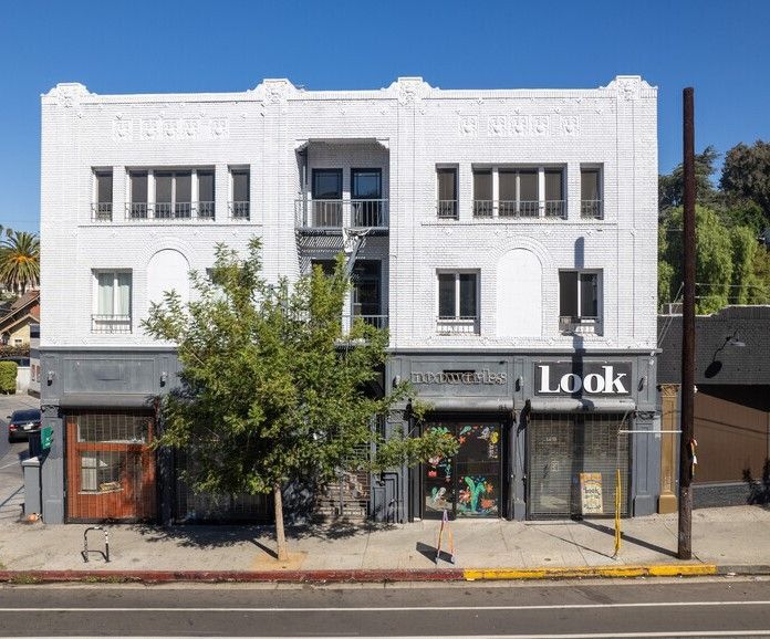 White stucco building with storefronts on street. Grey accents, tree in front, blue sky.