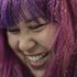 A close up of a woman with purple hair smiling.