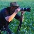 A man in a hat is taking a picture of a field with a camera.