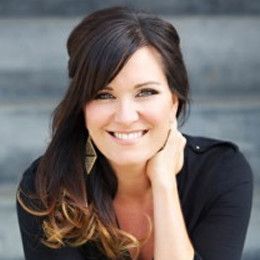 A woman in a black shirt is smiling with her hand on her chin.