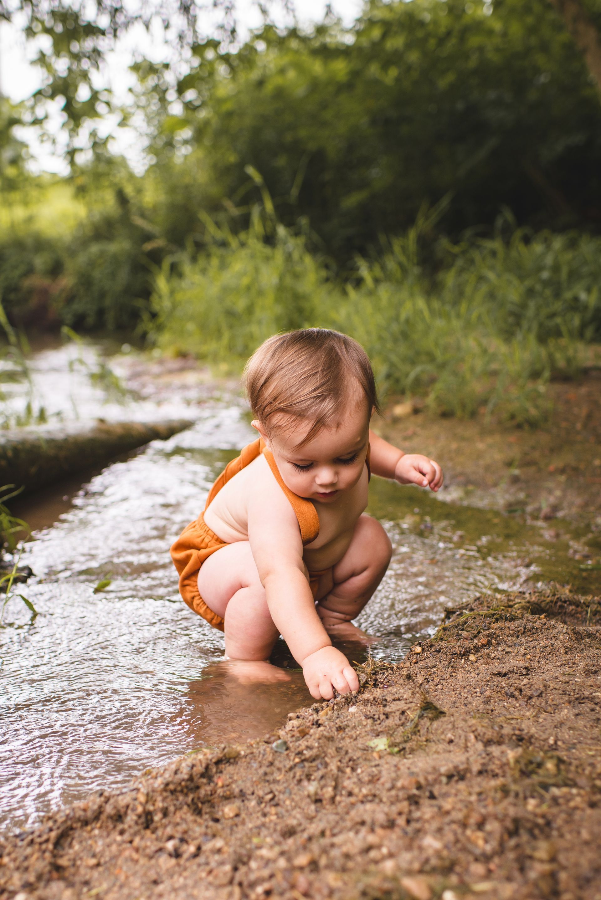 A baby is playing in a stream of water.