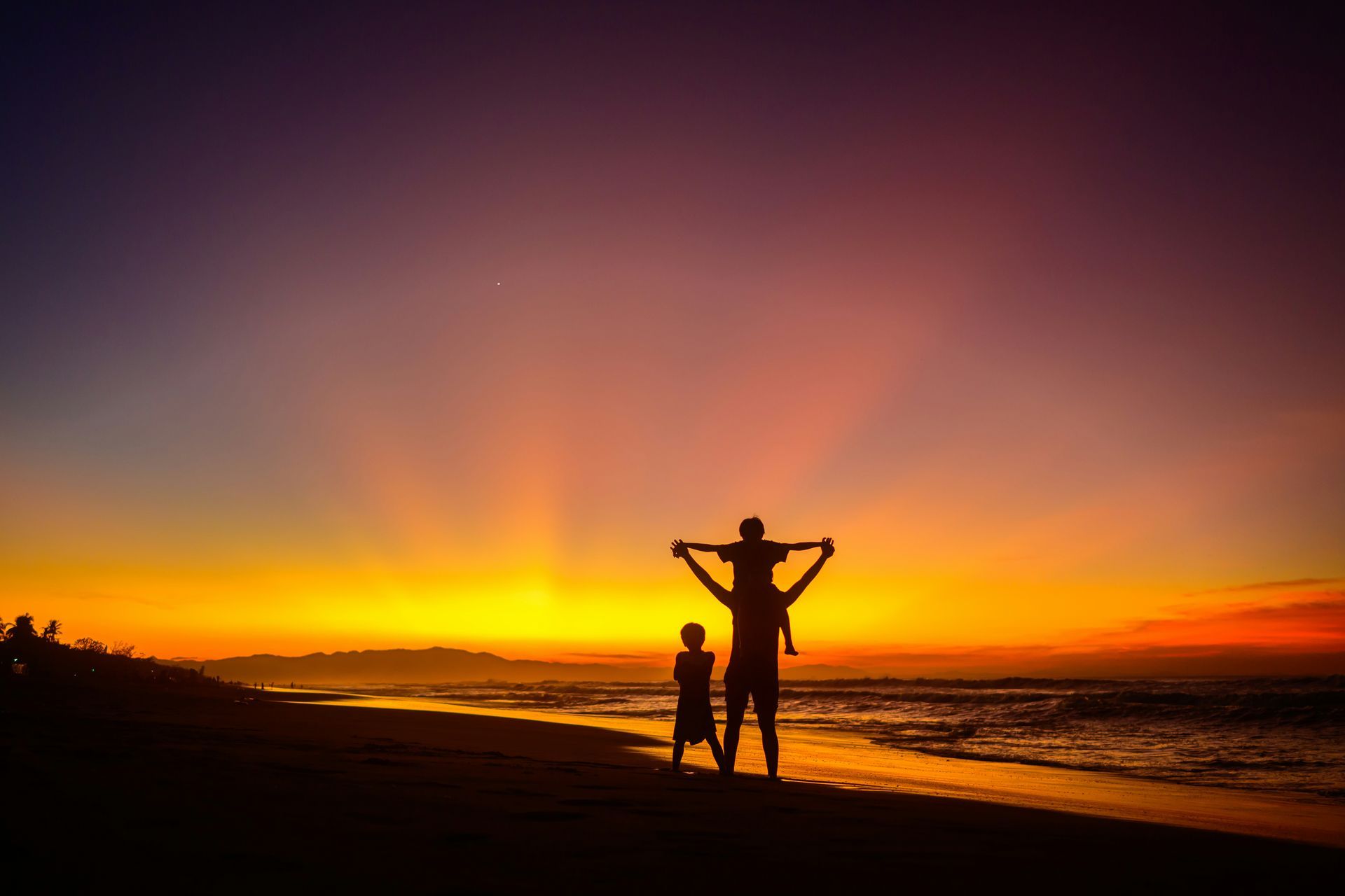 A man and a child are standing on a beach at sunset.