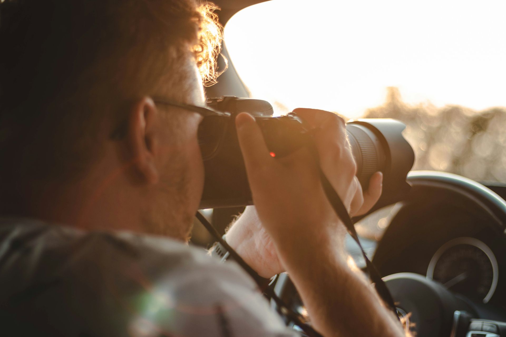 A man is sitting in a car taking a picture with a camera.