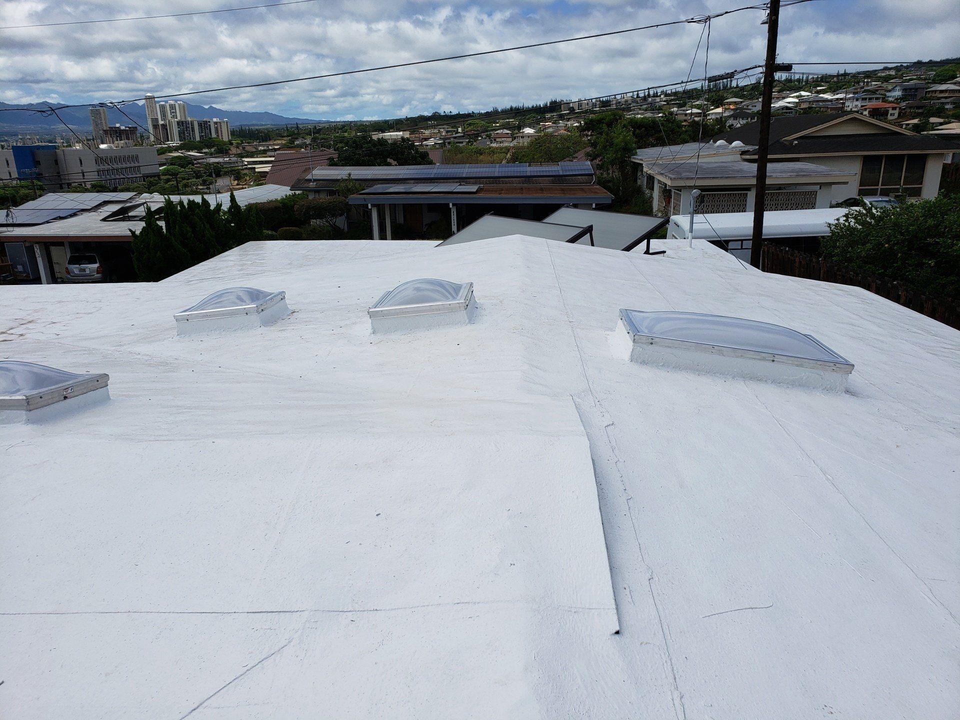 A white roof with skylights on it and a city in the background.