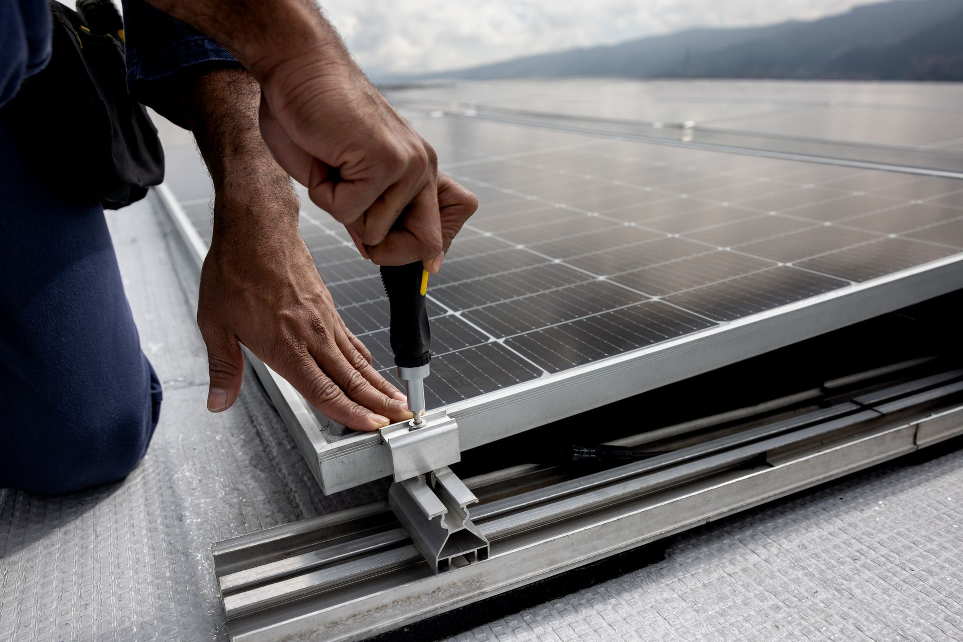 A man is installing a solar panel on a roof with a screwdriver.