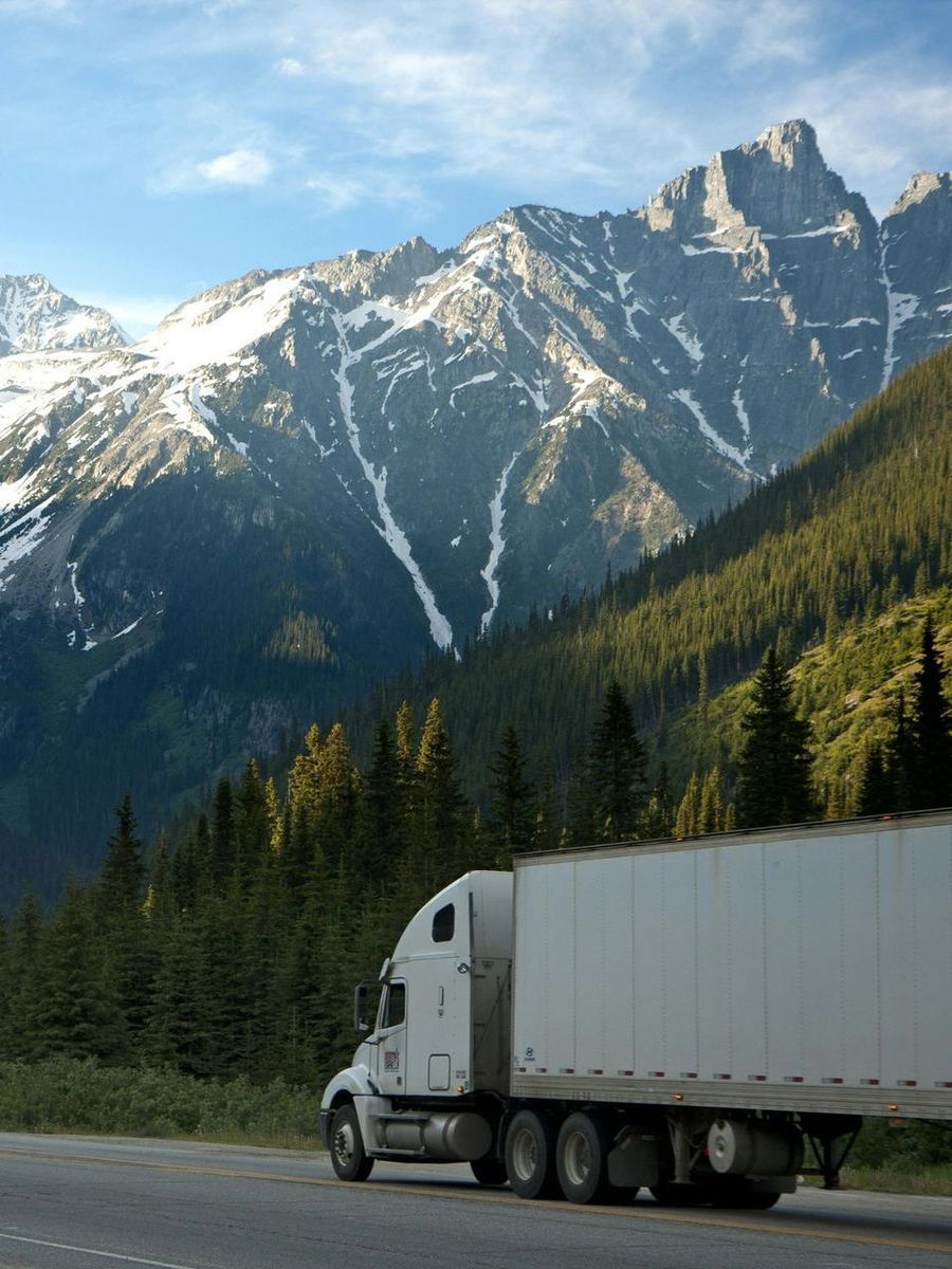 A semi truck is driving down a road with mountains in the background