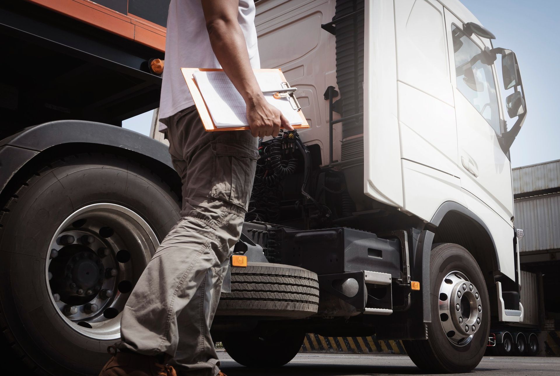 A man is standing next to a semi truck holding a clipboard.