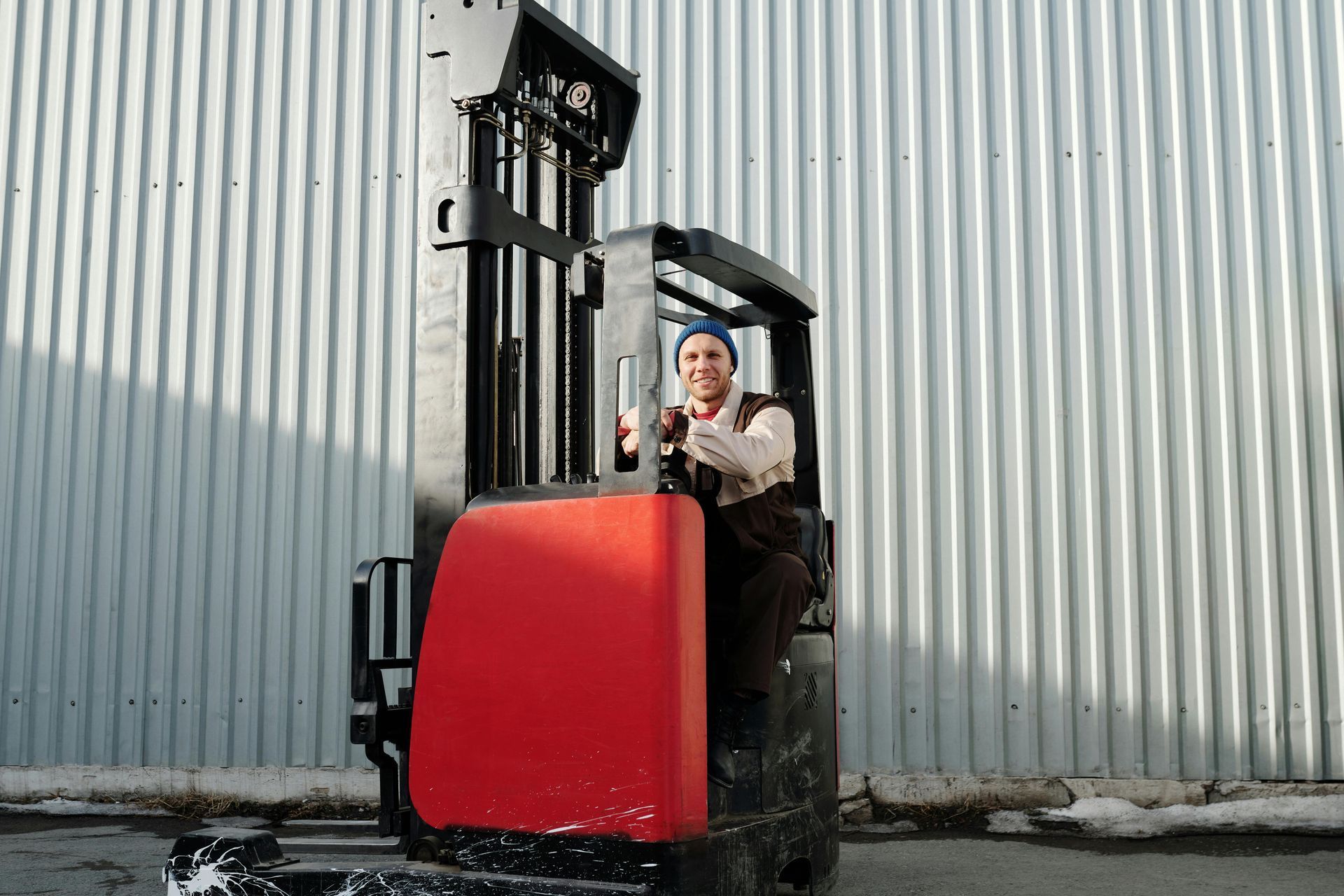 A man is driving a red forklift in front of a building.