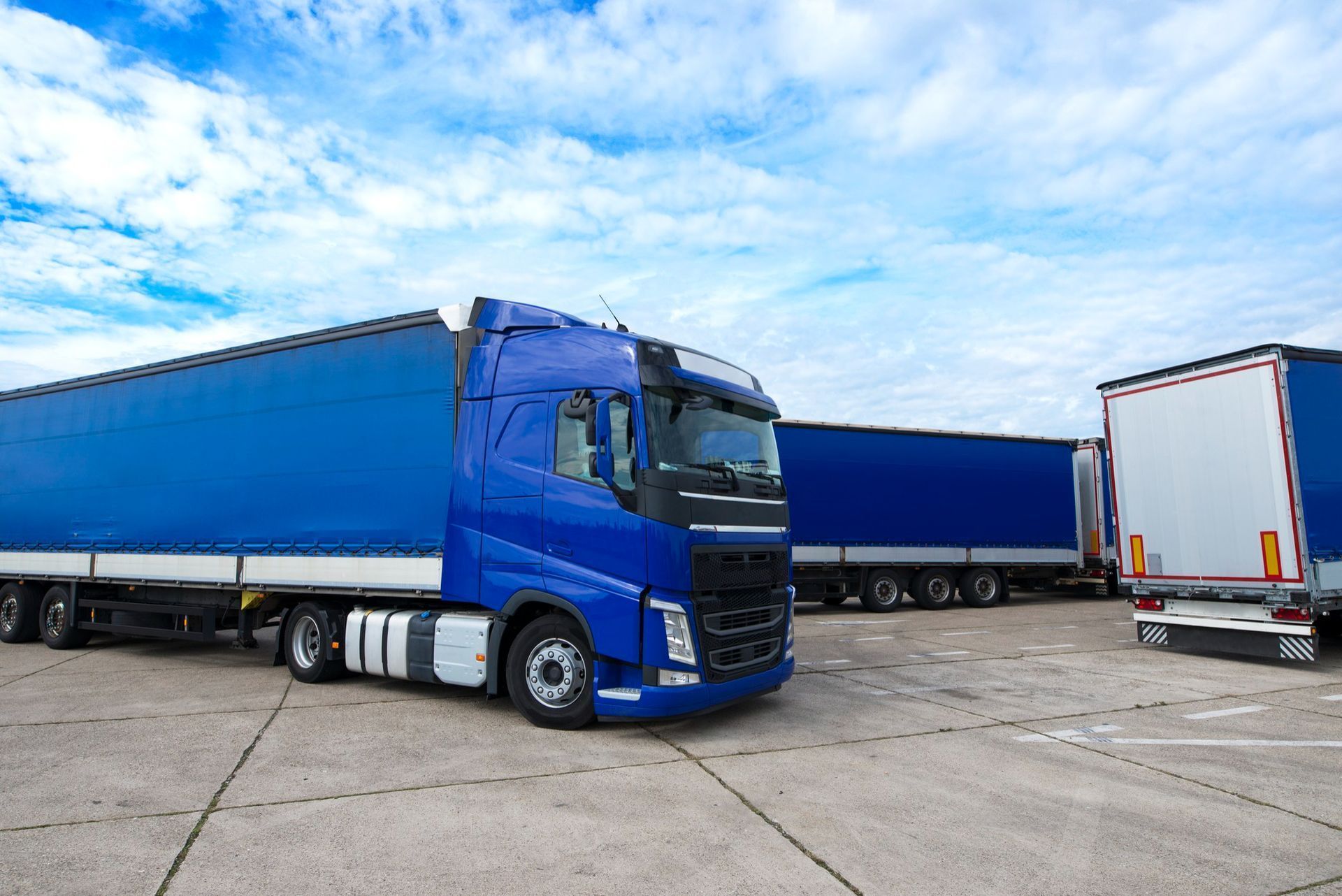 A blue semi truck is parked next to a white semi truck in a parking lot.