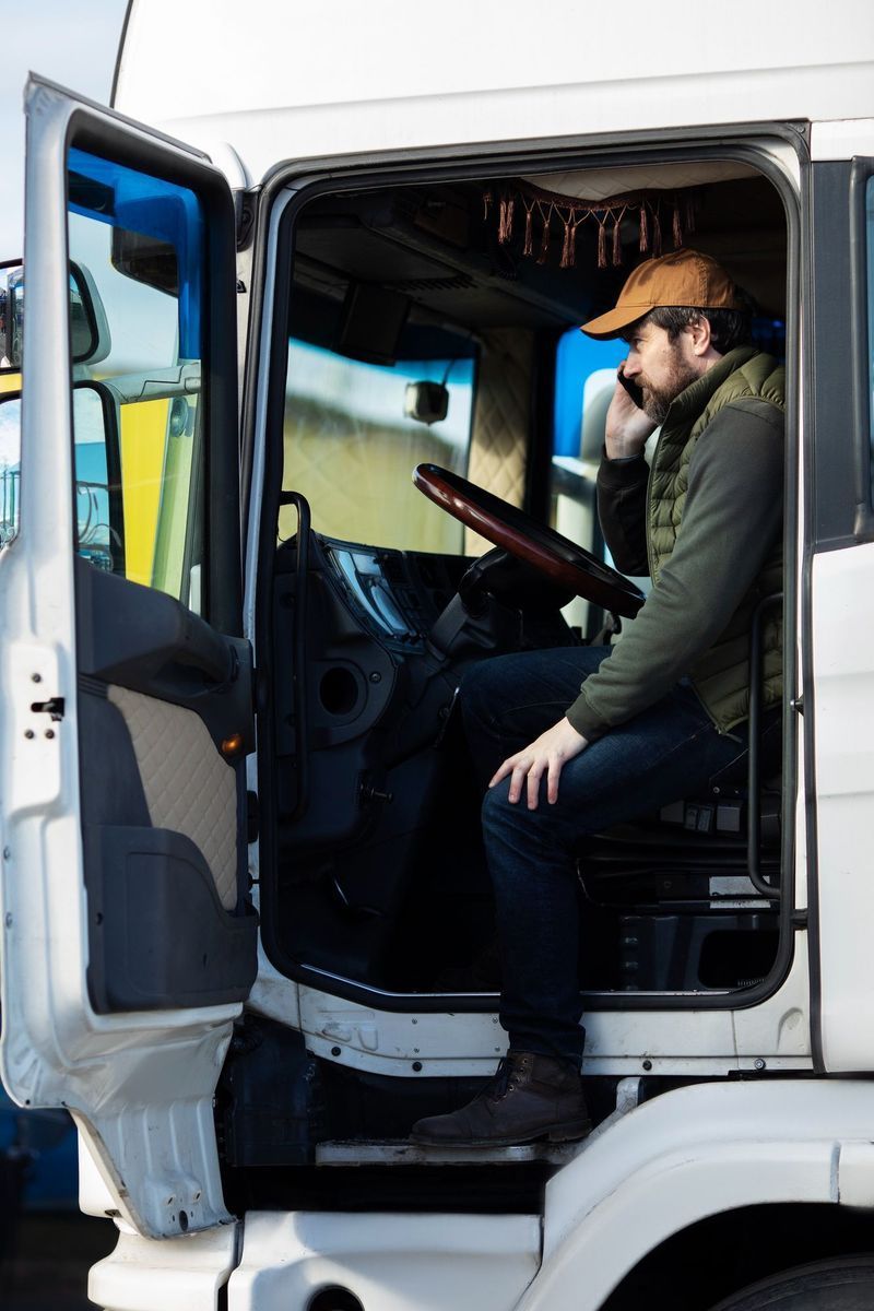 A man is sitting in the driver 's seat of a truck talking on a cell phone.