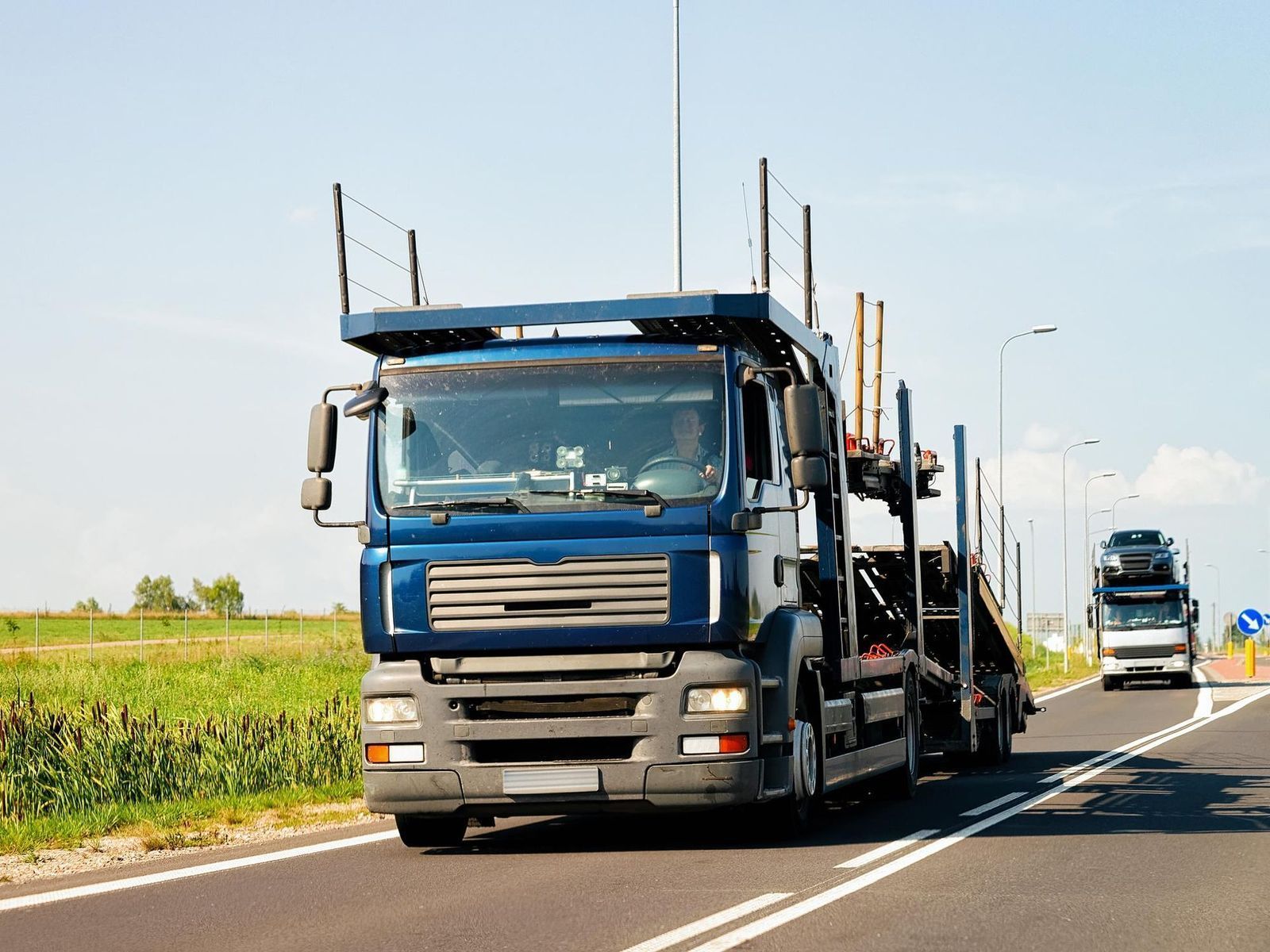 A blue truck is driving down a highway next to another truck.