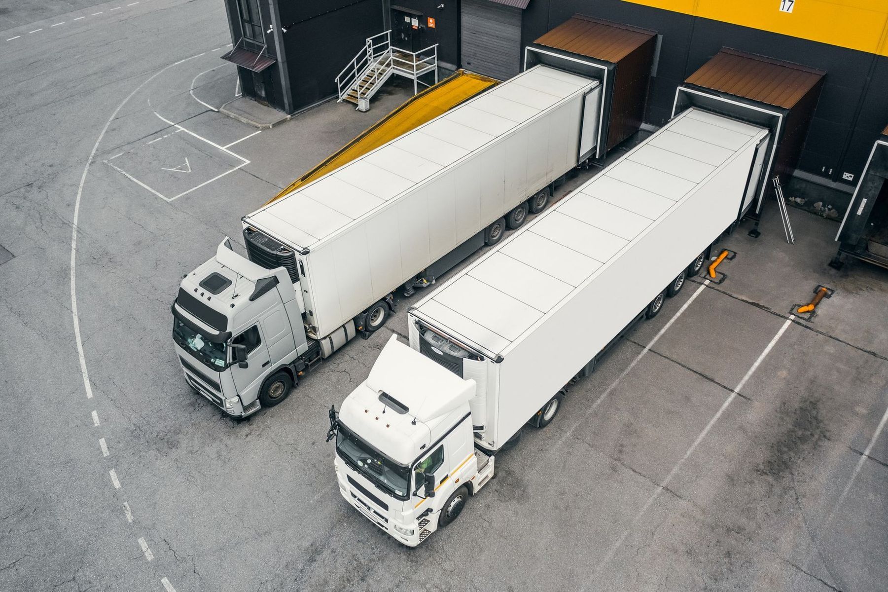 Two white semi trucks are parked in front of a warehouse.