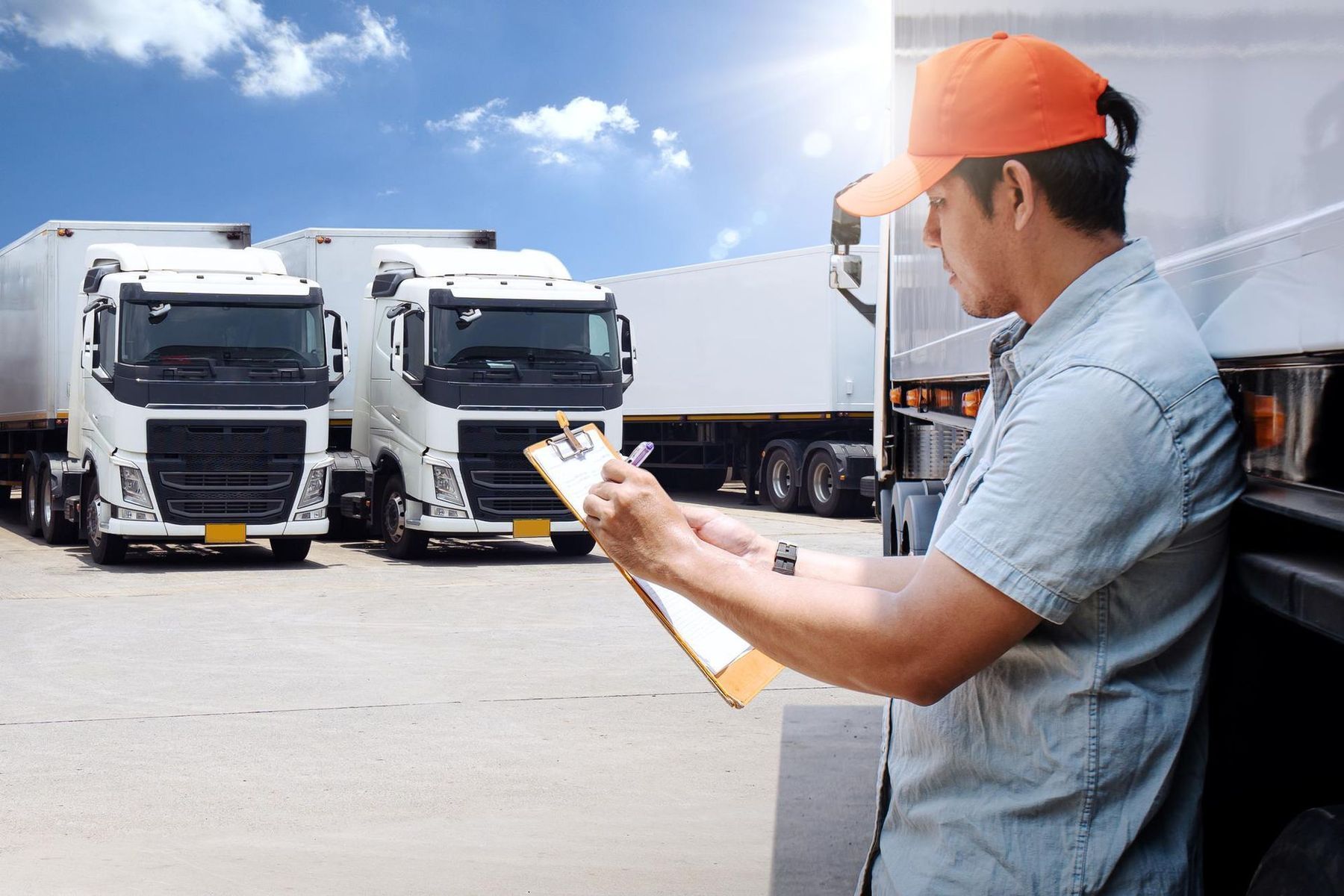 A man is writing on a clipboard in front of a row of trucks.