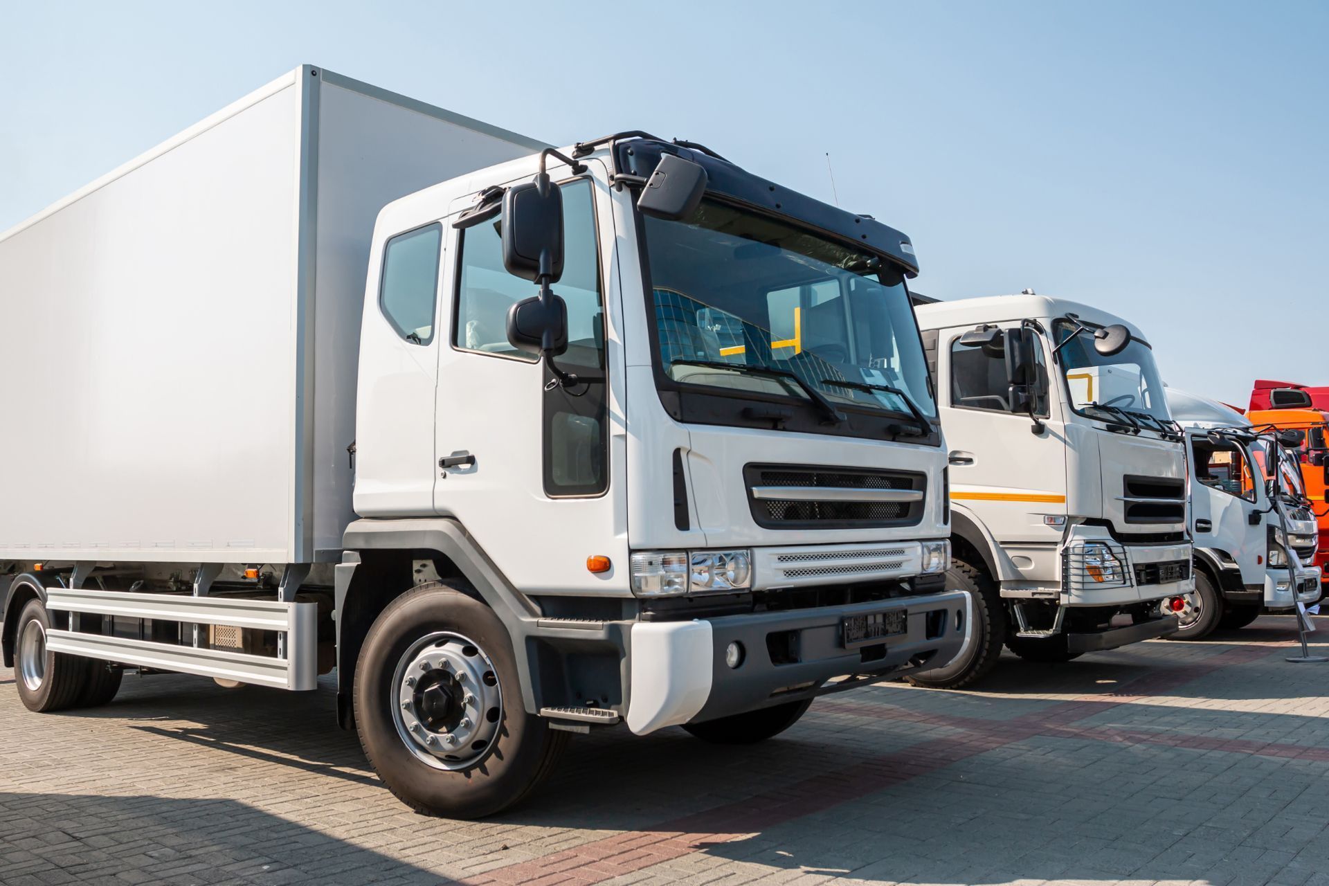 A row of white trucks are parked next to each other in a parking lot.
