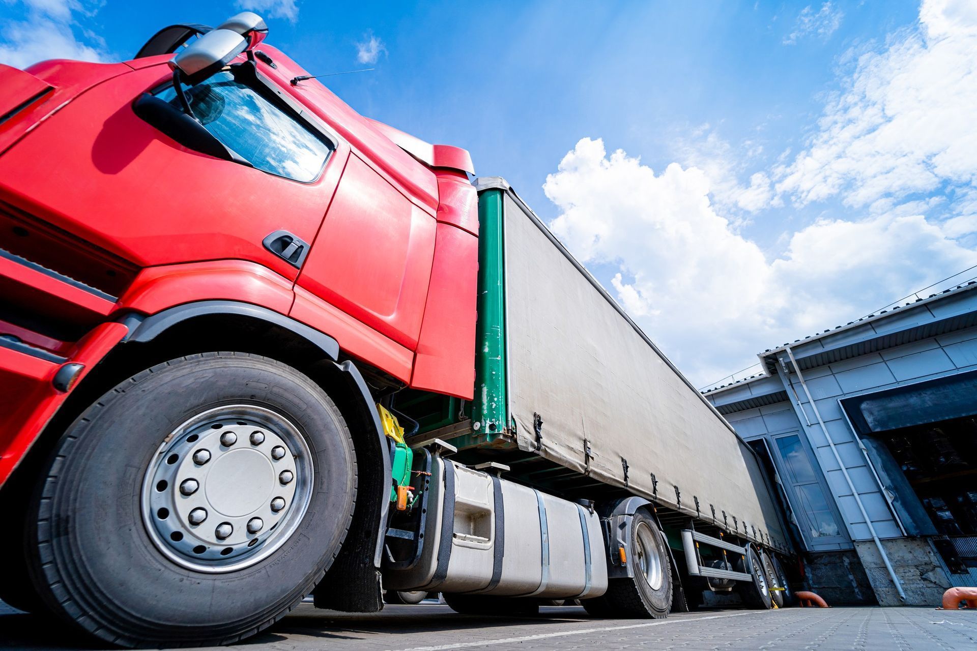 A red semi truck is parked in front of a warehouse.