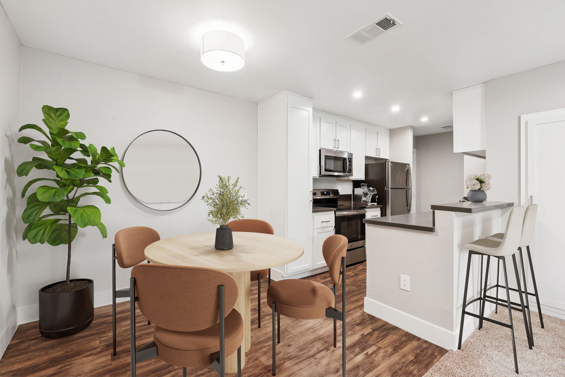 Open-concept apartment kitchen and dining area with white cabinets, stainless steel appliances, and a round dining table.