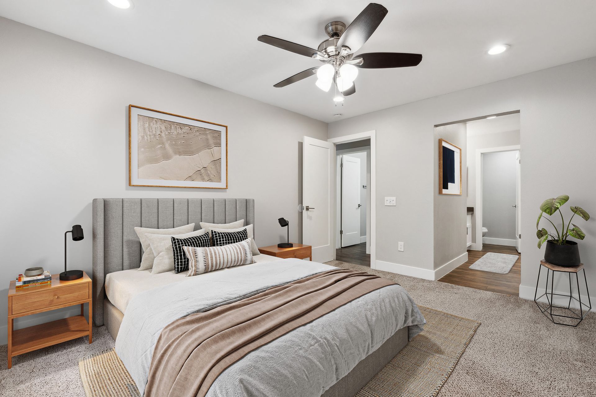Bedroom with gray upholstered headboard, two wooden nightstands, black lamps, and ceiling fan.