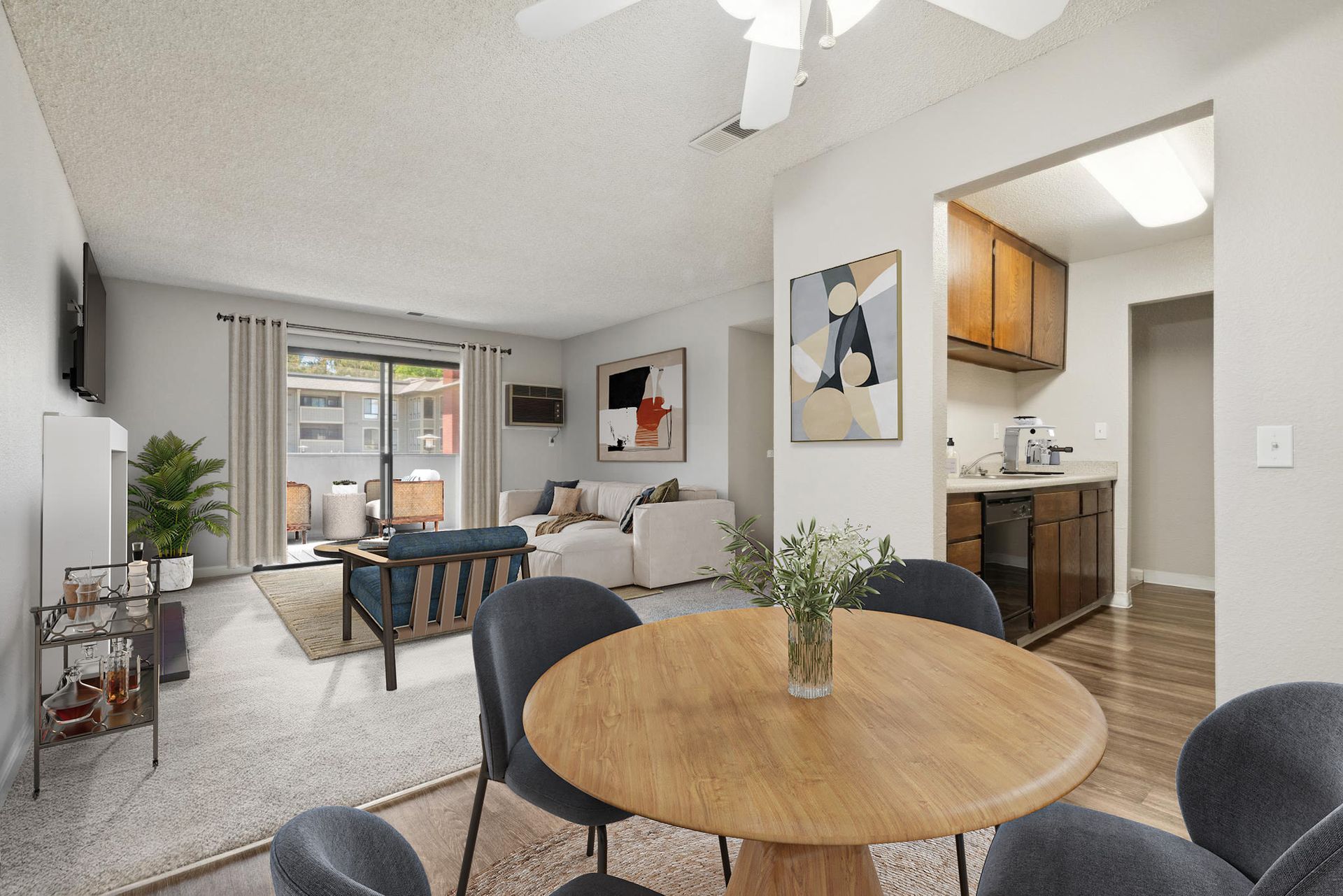 Open-concept apartment living area with round wooden dining table, sofa, and visible kitchen.
