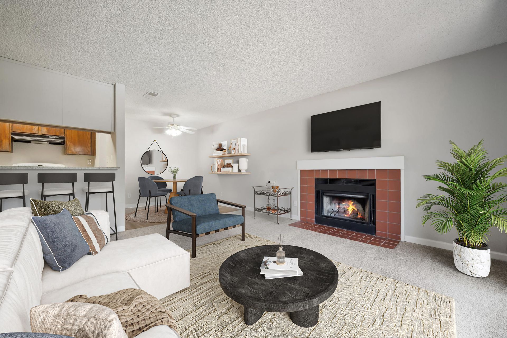 Living room with a fireplace, mounted TV, sofa and chairs, and an open kitchen with a breakfast bar.