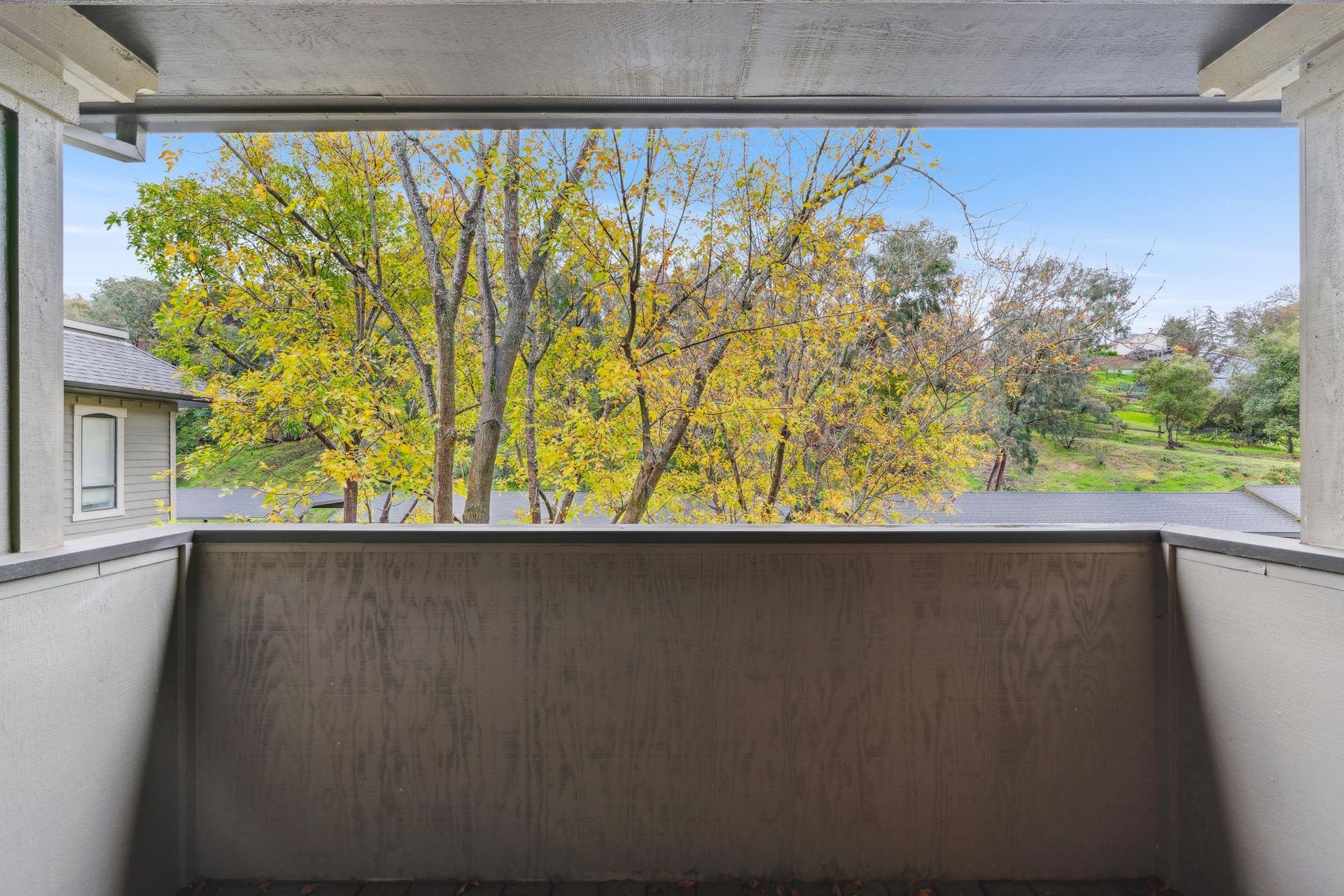 Balcony view from an apartment overlooking trees and autumn foliage.