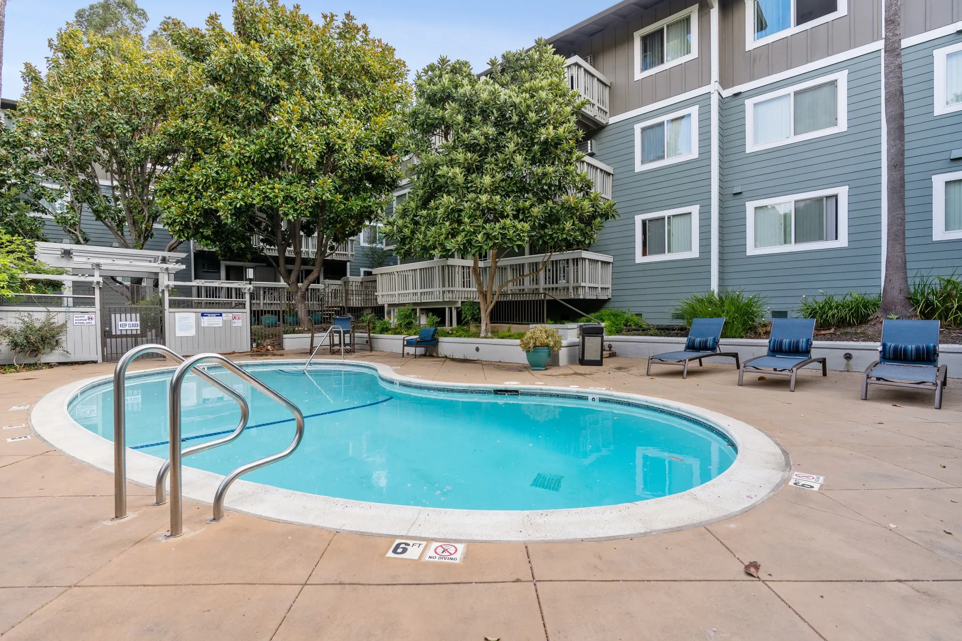 Outdoor apartment community pool with blue water, metal handrails, and surrounding lounge chairs.